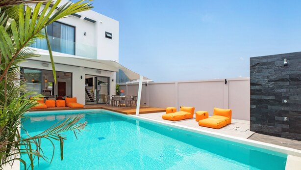 A modern pool area with a clear blue pool, orange loungers, and a contemporary building with large windows. - Boutique 5BR Oxygen Pool Villa Samakki 5 (Rawai)