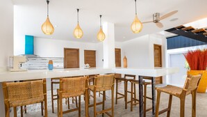 A modern kitchen with a white countertop, wooden chairs, and hanging pendant lights. - Boutique 5BR Oxygen Pool Villa Samakki 5 (Rawai)