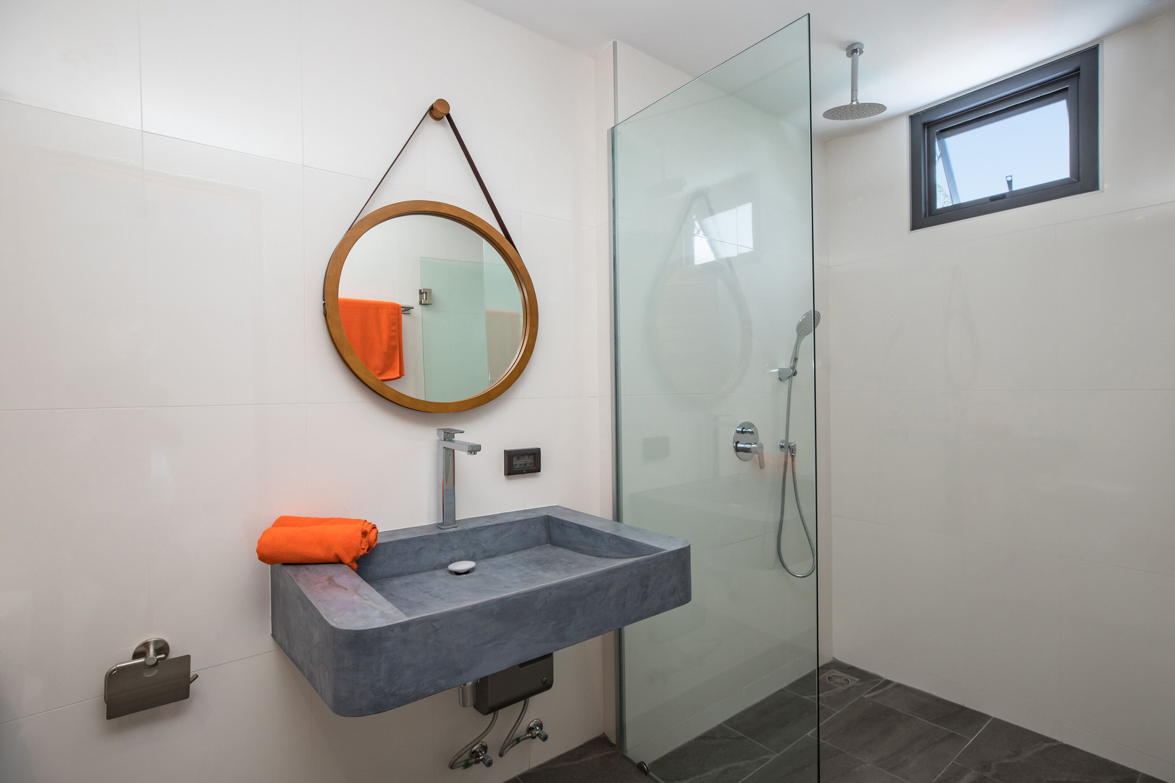 A modern bathroom with a glass shower enclosure, a built-in sink with a marble countertop, and a round mirror with a wooden frame.
