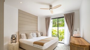 A modern bedroom with a large bed, a ceiling fan, and a view of greenery outside. - Boutique 5BR Oxygen Pool Villa Samakki 5 (Rawai)
