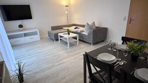 Una sala de estar moderna con un sofá gris, una mesa de centro blanca y un comedor con una mesa negra para cuatro personas.