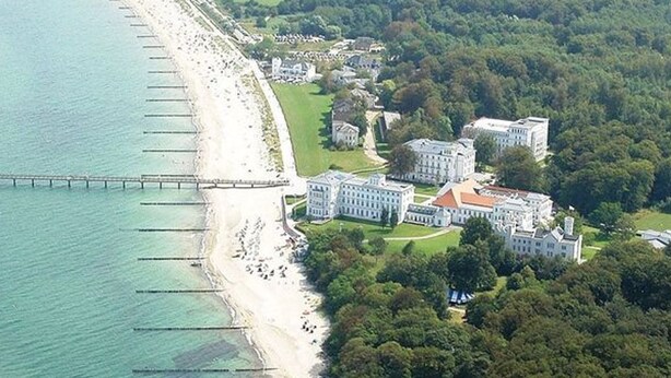 Vista aérea de un complejo turístico costero con playa, muelle y varios edificios grandes.