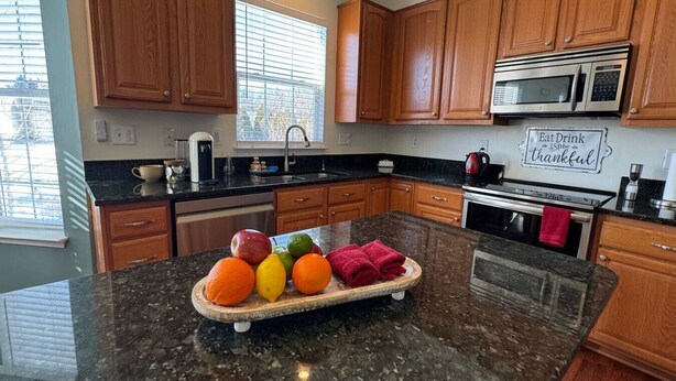 A kitchen with wooden cabinets, a granite countertop, a microwave, and a sign that says "Eat Drink Be thankful". - Colonial Playland - 5BD, Private Yard, Game Room (Manassas)