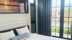 A hotel room with a large bed, a painting on the wall, and a view of the outdoors through a window. - Deluxe 3 Br Corner House - Novaworld PT (Tien Thanh)