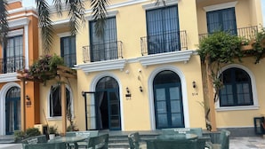 A yellow building with numbered doors and windows, outdoor seating with benches, and a palm tree. - Deluxe 3 Br Corner House - Novaworld PT (Tien Thanh)