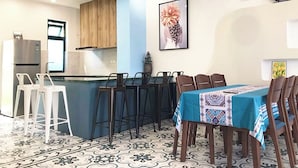 A kitchen with a blue island, wooden cabinets, a refrigerator, and a dining area with chairs and a table. - Deluxe 3 Br Corner House - Novaworld PT (Tien Thanh)