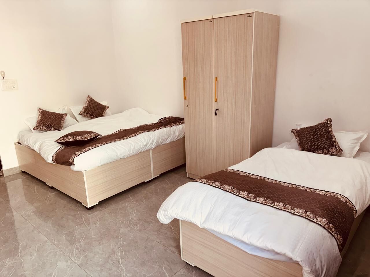 A bedroom with two beds, a wardrobe, and a tiled floor.