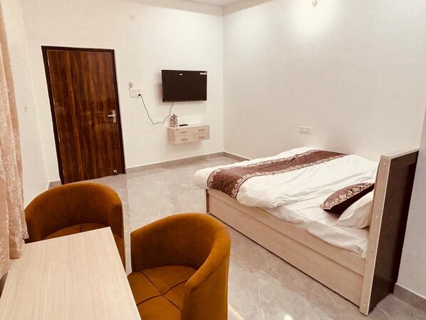 Un dormitorio con una cama, un televisor montado en la pared, un escritorio y dos sillas.