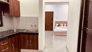 Eine moderne Küche mit dunklen Holzschränken und einer schwarzen Arbeitsplatte, die zu einem Schlafzimmer mit Holztür und einem Bett mit weißer Bettwäsche führt.