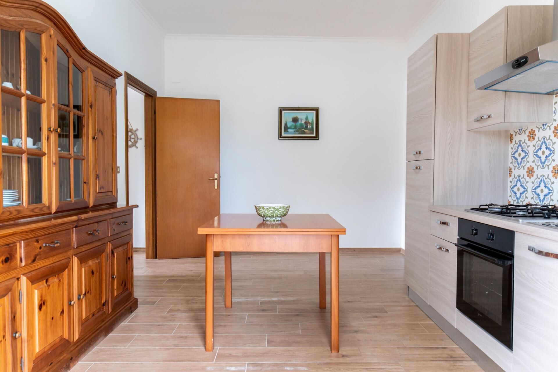 Uma cozinha com mesa de madeira, armários, fogão e uma porta que dá para outro cômodo.