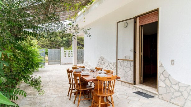 A patio with a table and chairs, a covered area, and a stone wall.