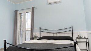 Un dormitorio con una cama, una ventana con cortinas, aire acondicionado instalado en la pared y una mesita de noche.