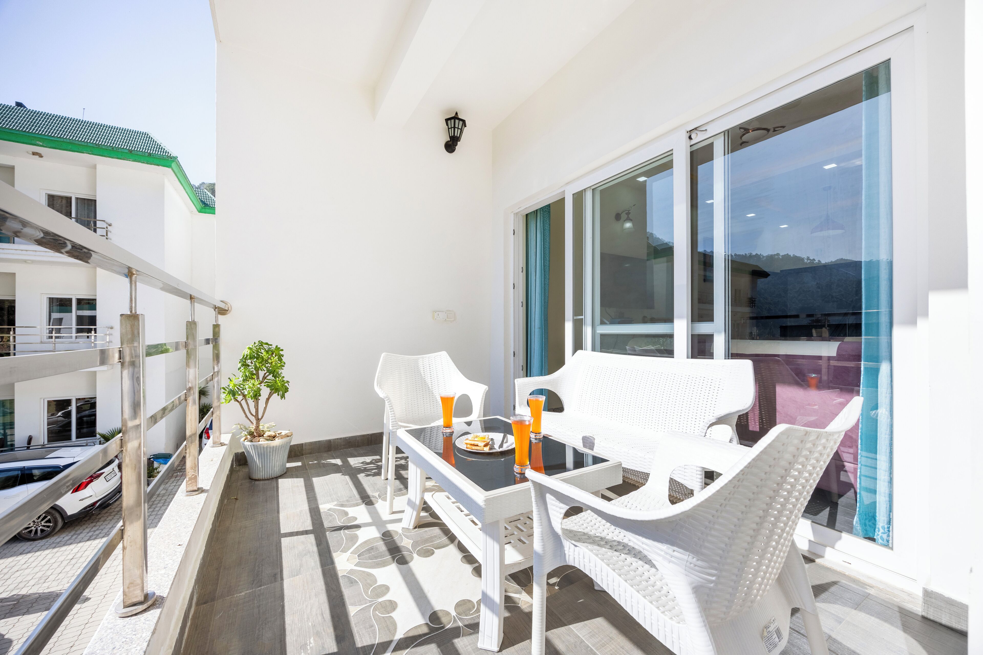 Ein Balkon mit weißen Korbmöbeln, einem Topfpflanzen und einem Tisch mit zwei orangen Getränken.