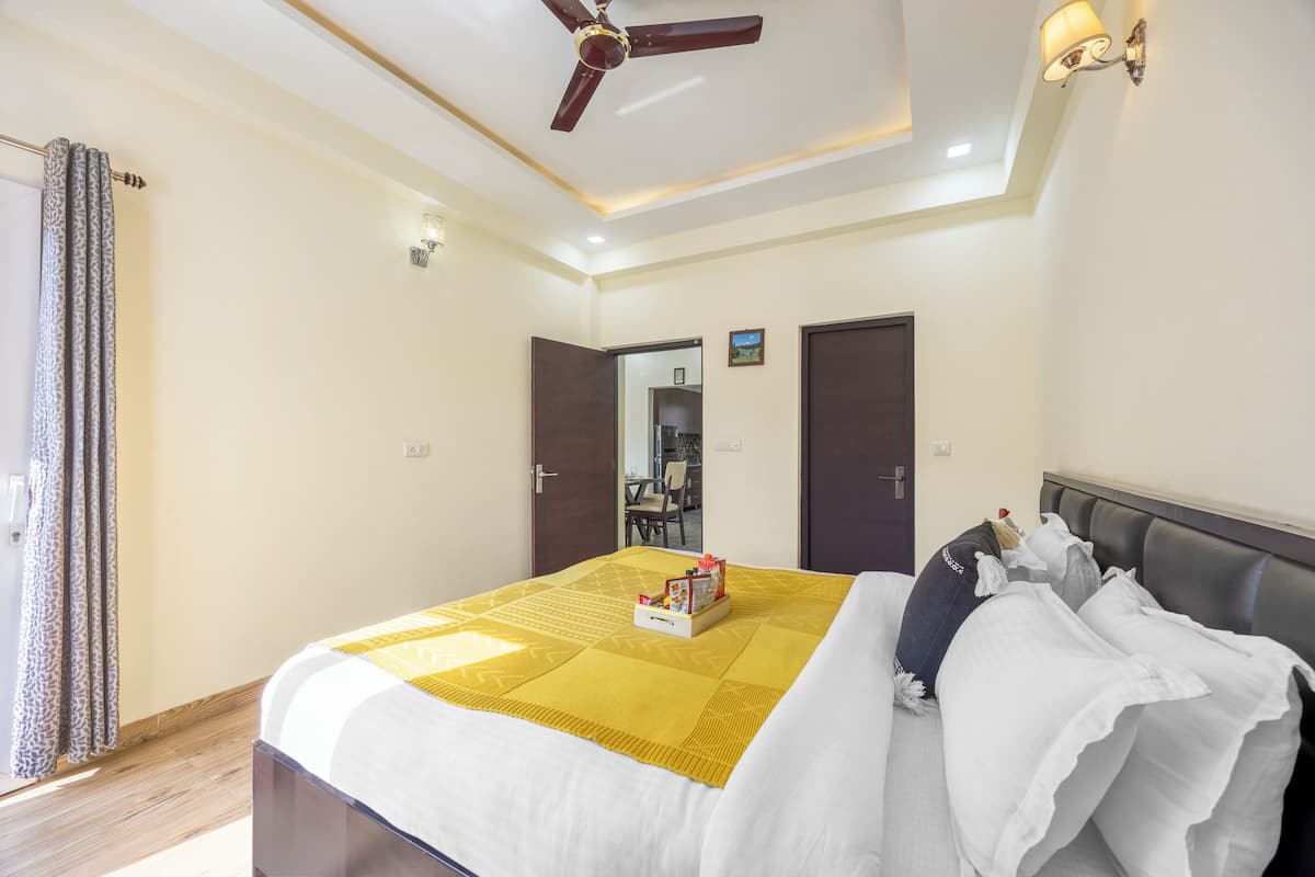 Une chambre d’hôtel avec un lit, un ventilateur de plafond, une table de chevet et une vue sur le couloir.