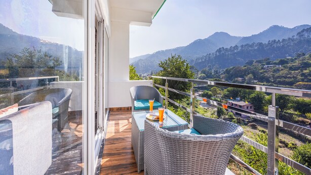 A balcony with wicker furniture, a glass table, and a view of mountains and greenery.