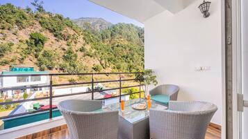 Un balcon avec des fauteuils en osier, une table en verre et une vue sur une piscine et la verdure.
