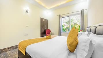A hotel room with a bed, a red chair, a fruit basket, and a window with a view of greenery.