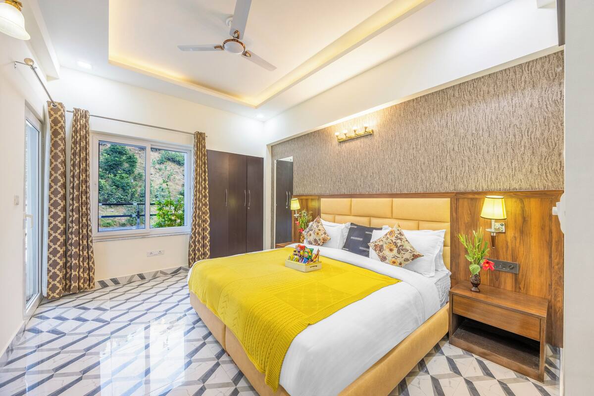 Une chambre d’hôtel avec un grand lit, une table de chevet, un ventilateur de plafond et une fenêtre avec des rideaux.