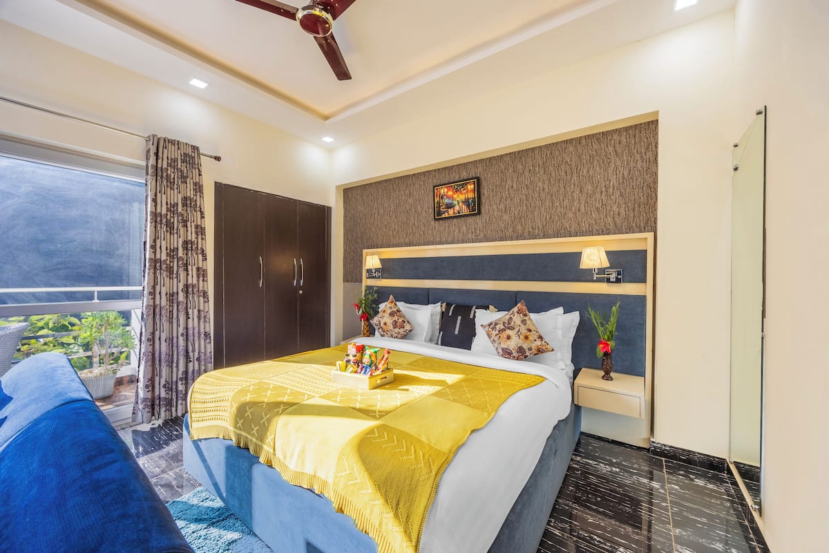Une chambre d’hôtel avec un lit, une table de chevet, une lampe, une œuvre d’art murale et une vue sur la verdure à l’extérieur.