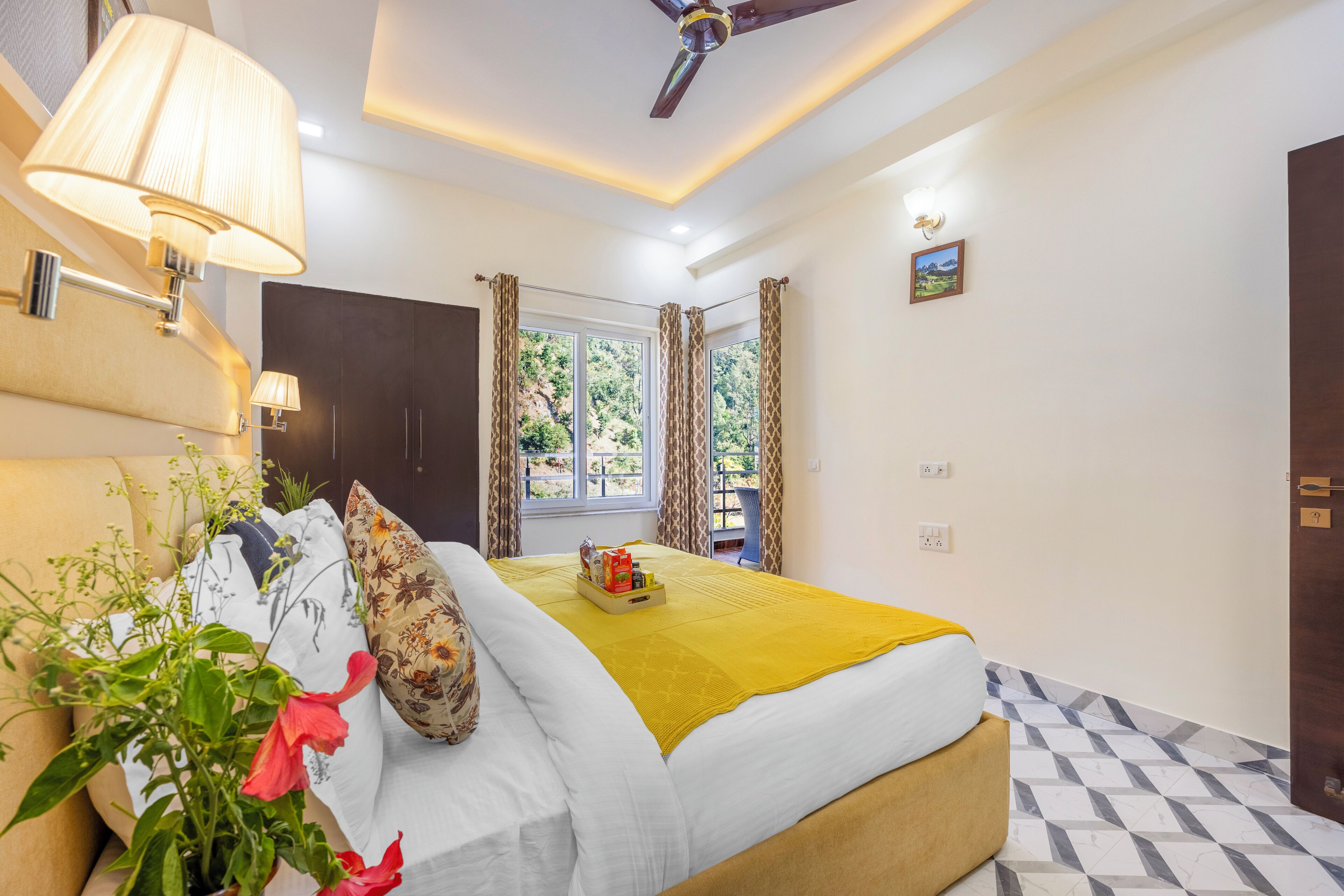 Ein Hotelzimmer mit Bett, Deckenventilator, Fenster mit Vorhängen, Nachttisch und Wandlampe.