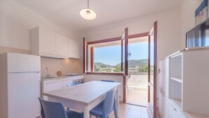 A compact kitchen with white cabinets, a dining table with blue chairs, and a view of the outdoors through a large window.