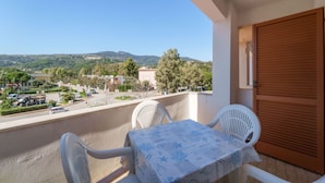 A balcony with a table and chairs, overlooking a residential area with houses and trees, and a mountain in the distance.