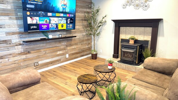A modern living room with a flat-screen TV mounted on a wooden wall, a fireplace, leather sofas, a coffee table, and a potted plant.