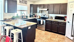 A modern kitchen with dark wood cabinets, a granite island, stainless steel appliances, and a tiled floor.