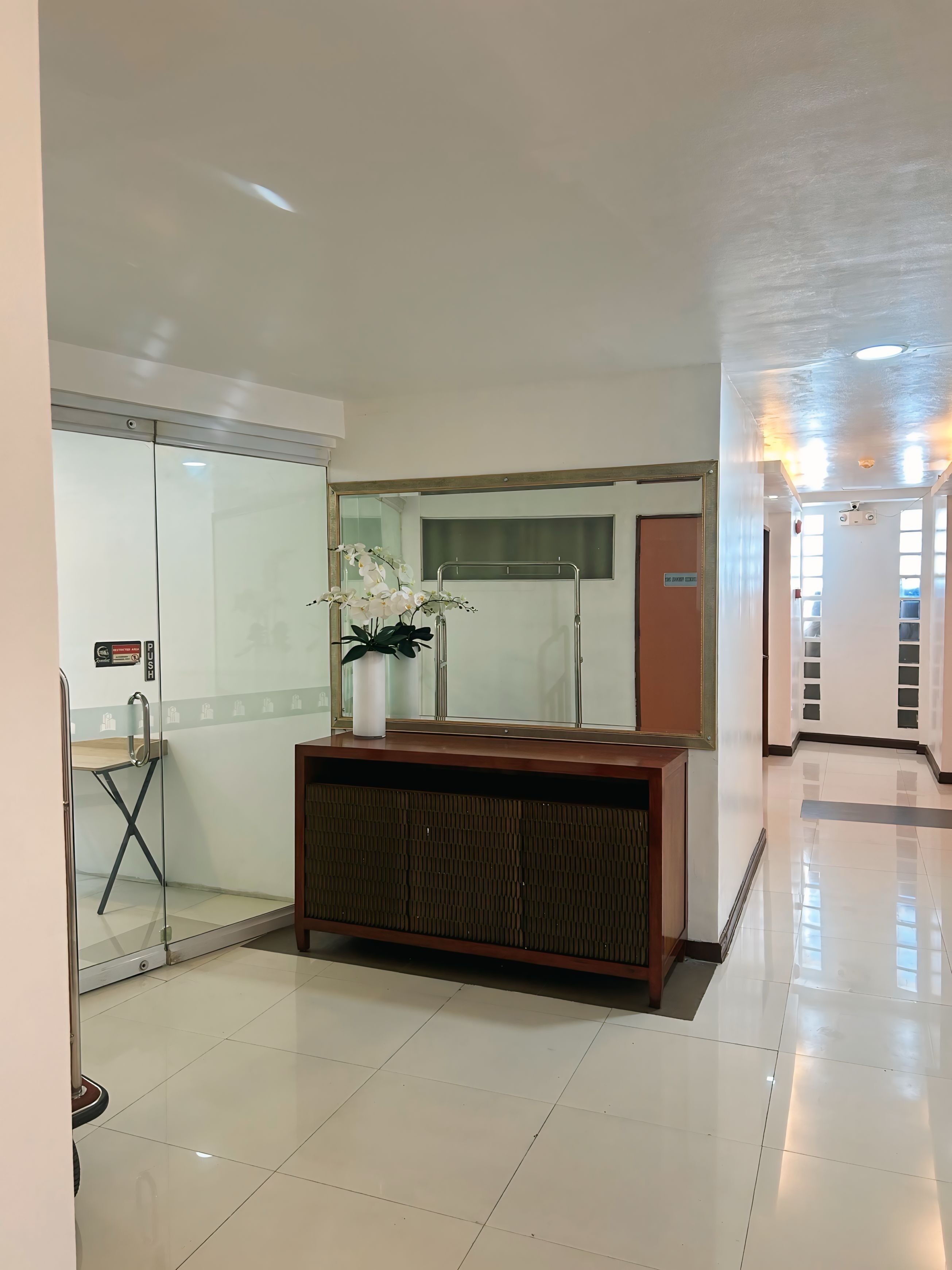 A modern hotel lobby with a glass partition, a wooden reception desk, and a potted orchid.