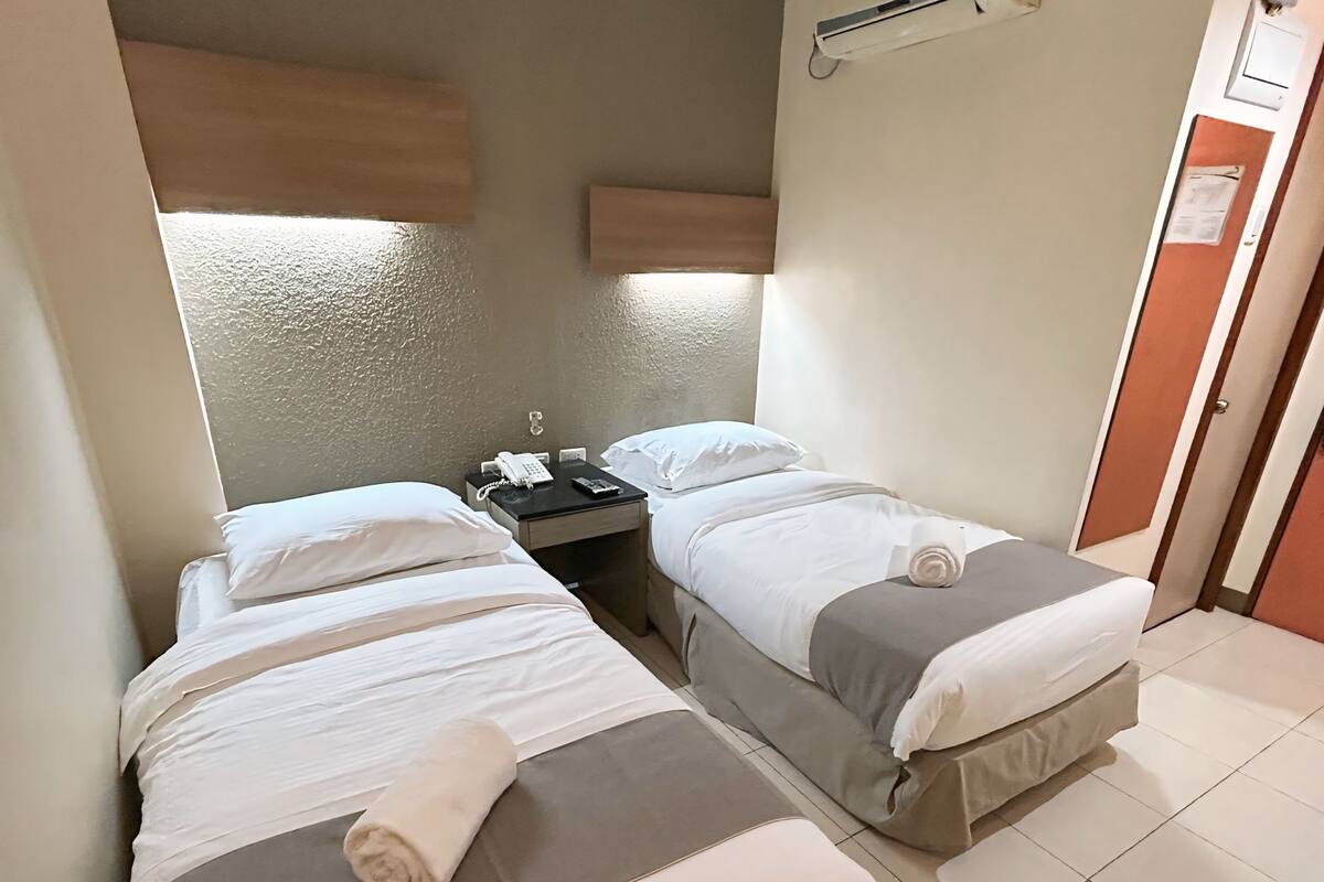 Habitación de hotel con dos camas, una mesita de noche con teléfono y un equipo de aire acondicionado en la pared.