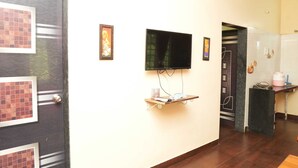 Habitación de hotel con televisor montado en la pared, un estante pequeño con un control remoto y una puerta con un diseño decorativo.