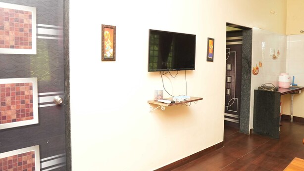 A hotel room with a TV mounted on the wall, a small shelf with a remote control, and a door with a decorative pattern.