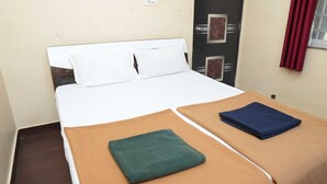 Una cama individual con ropa de cama blanca, una manta marrón y una toalla azul sobre un piso de madera.