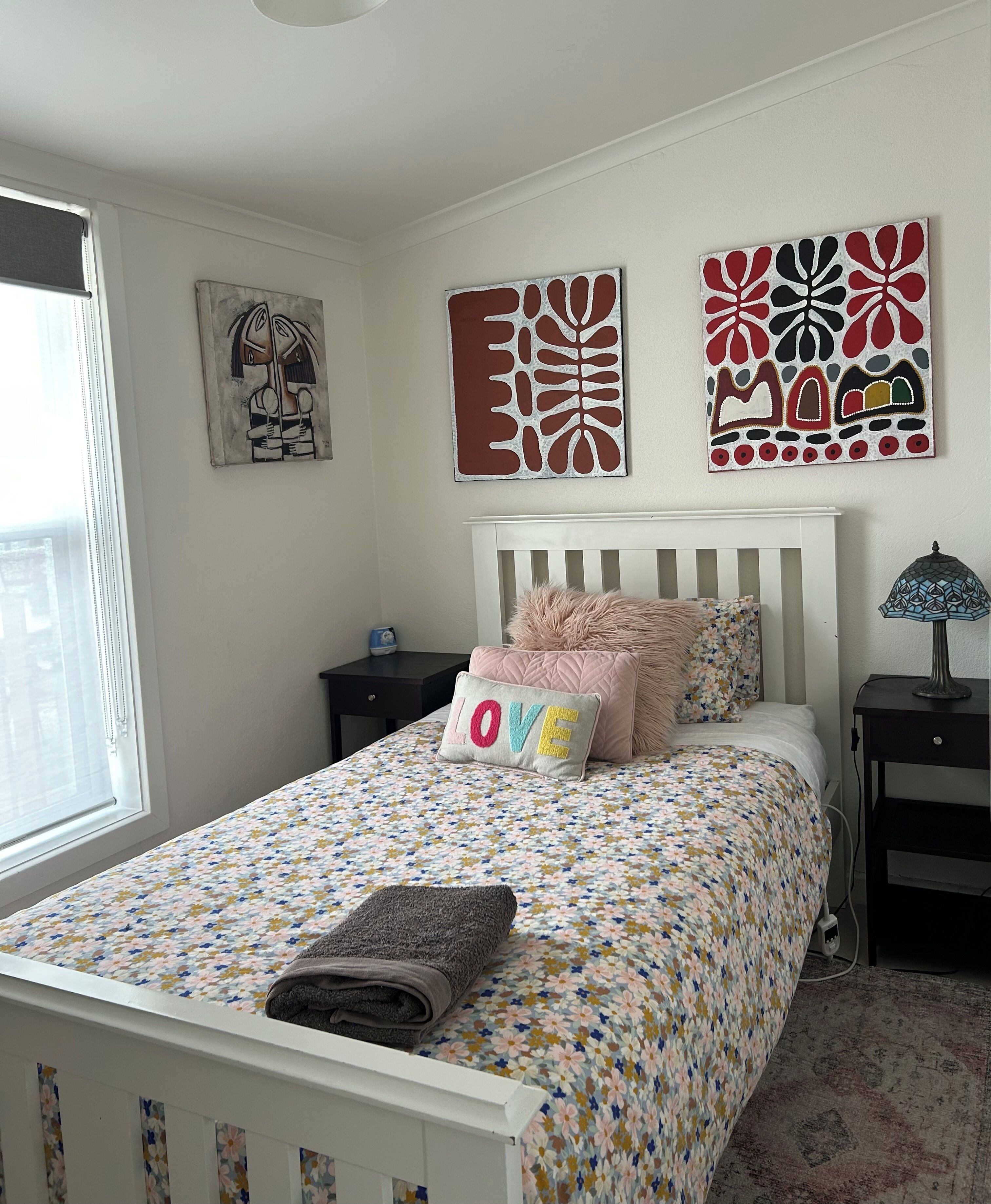 Een slaapkamer met een bed, kussens, een nachtkastje en wanddecoratie.
