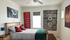 A bedroom with a bed, wooden nightstands, a ceiling fan, and artwork on the walls.
