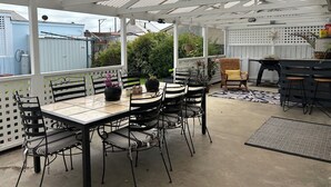 A covered patio area with a table and chairs, a grill, and potted plants.