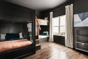 Quarto compacto com beliche, uma pequena escrivaninha e janela com cortinas.