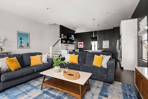 Uma sala de estar moderna com um sofá cinza, almofadas amarelas, uma mesa de centro de madeira e um tapete azul estampado.