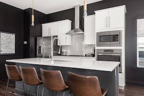 Uma cozinha moderna com ilha central, eletrodomésticos de aço inoxidável e disposição de banquetas.