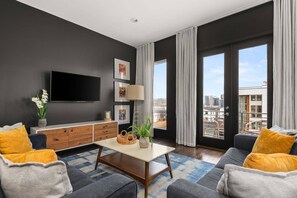 A modern living room with a flat-screen TV, artwork, a coffee table, and a sofa with cushions. - A19 ~ 12 Beds ~ 4 Suites ~ New Listing in The Gulch ~ Garage Parking ~ City Views ~ Fresh and Clean (Nashville)