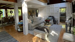 A spacious living area with a high ceiling, wooden beams, a large sofa set, and a dining area with a table and chairs.