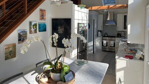 A modern kitchen with white cabinets, stainless steel appliances, and a dining area with a marble table and orchid flowers.