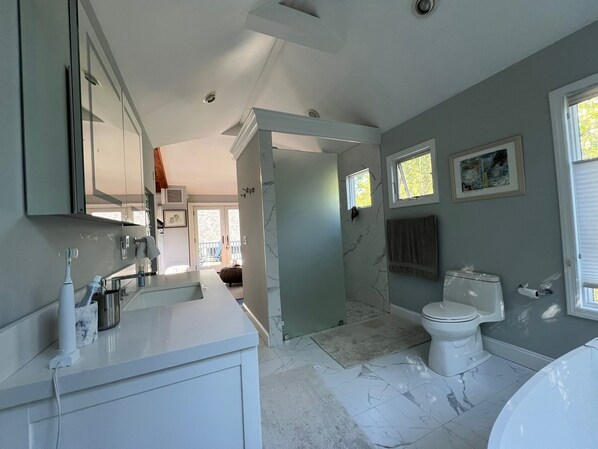 A modern bathroom with a white sink, a toilet, and a bathtub. There is a window providing natural light and a door leading to another room.