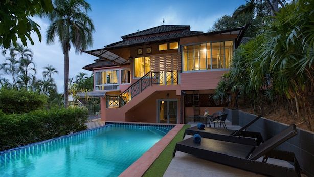 A two-story house with a swimming pool, a balcony, and a patio area with lounge chairs.