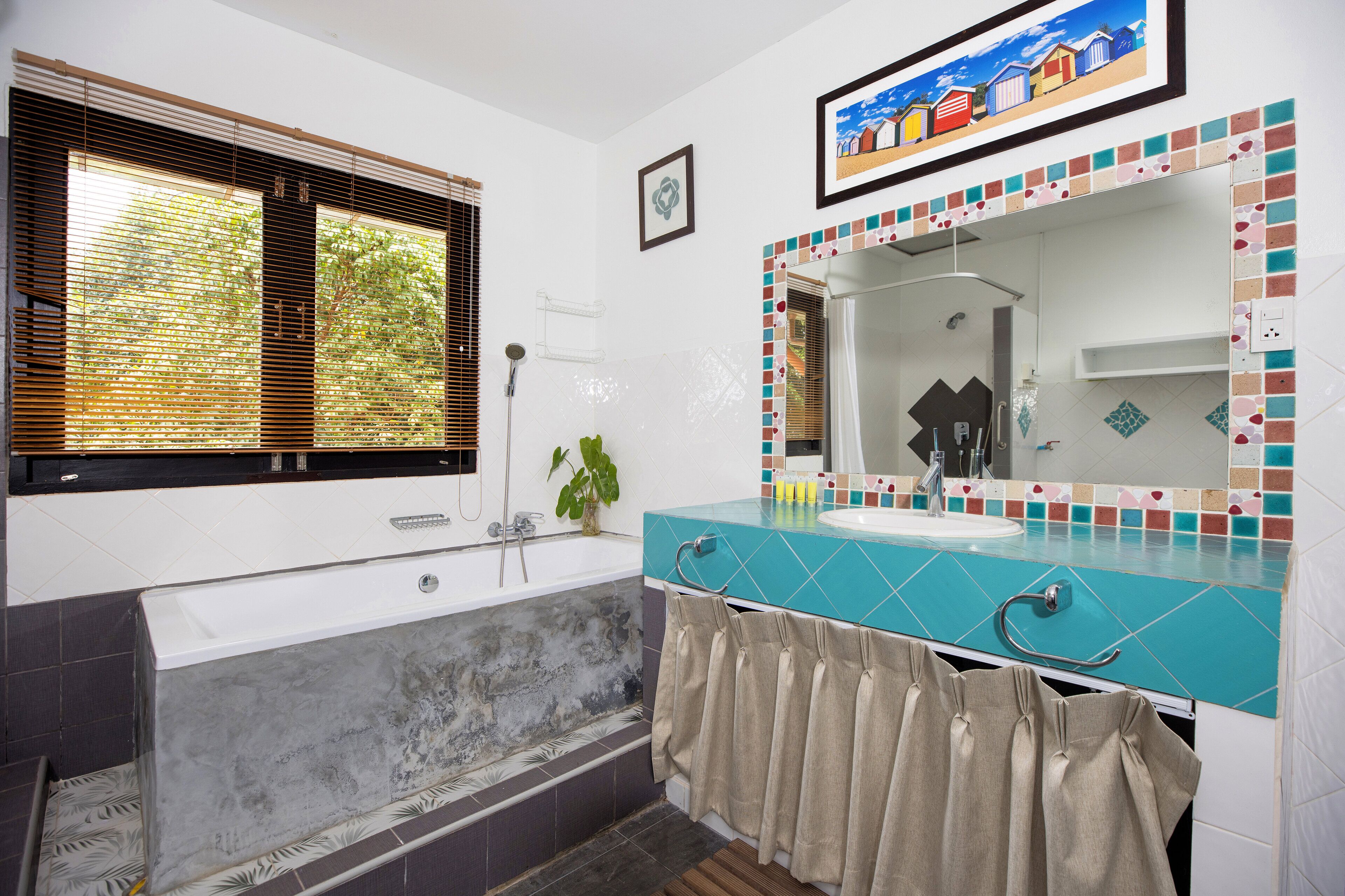 A bathroom with a bathtub, a sink, and a shower. There is a window with blinds and a plant on the windowsill.