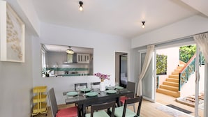 A dining area with a table set for four, a kitchen in the background, and a staircase leading to an outdoor area.