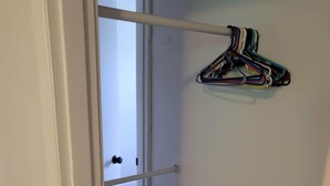 A hallway with a white door leading to a room. A white metal rod is mounted on the wall, and a set of colorful hangers is attached to it.