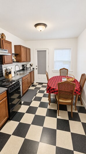 A compact kitchen with a dining area, featuring a checkered floor, wooden cabinets, and a table set for two.