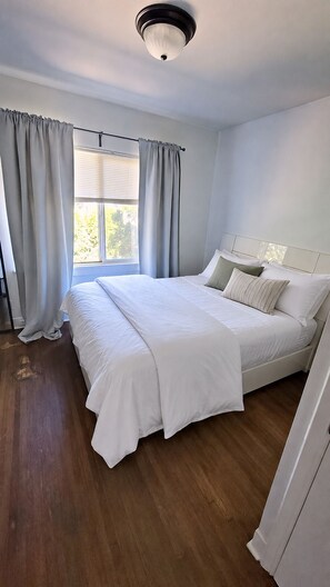 Quarto com cama grande, janela com cortinas e luminária no teto.