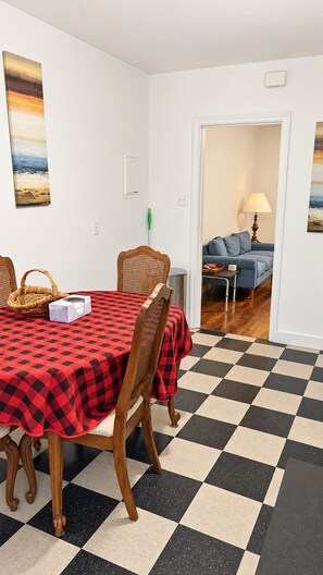 Uma área de refeições com toalha de mesa xadrez, cadeiras de madeira e chão quadriculado.